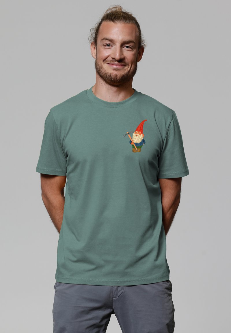 Grünes Baumwoll-T-Shirt mit einer Gnom-Grafik, der einen roten Hut, ein blaues Hemd und Werkzeuge trägt. Das Shirt ist mit einem Rundhalsausschnitt und kurzen Ärmeln gestaltet.