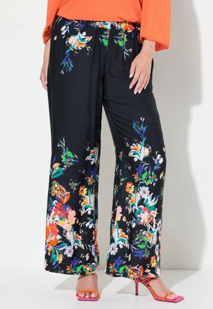 Pantalones de pierna ancha negros con patrones florales multicolores vibrantes, cinturilla elástica y tela suave. Combinados con tacones rosas.