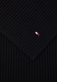 Écharpe en tricot côtelé noir avec un design triangulaire et un petit logo brodé en rouge, blanc et bleu sur un côté.