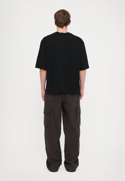 Schwarzes oversized T-Shirt und dunkle Cargo-Hosen. Das Shirt hat kurze Ärmel und einen Rundhalsausschnitt; die Hosen verfügen über Seitentaschen und eine lockere Passform.
