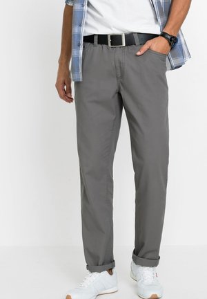 Pantaloni grigi in cotone misto con una vestibilità rilassata, orli risvoltati e vita elasticizzata, abbinati a una cintura nera e scarpe da ginnastica bianche.