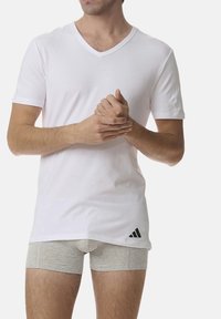 White v-neck t-shirt with short sleeves, made of cotton; paired with light gray boxer shorts featuring a black adidas logo on the side.