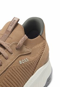 Brun sneaker med strukturerad nätöverdel, grå detaljer och logotyp. Rundad form, vadderad sula med vit kant och mönstrat grepp.