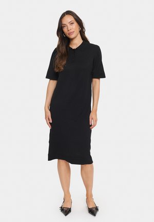 Vestido negro de algodón con cuello de polo, mangas cortas y silueta recta, que presenta un dobladillo a la altura de la rodilla y detalles acanalados en la parte inferior.