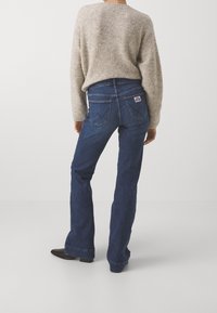 Mörkblå utsvängda jeans i denim, med hög midja, dubbla bakfickor med logodetalj och en ren fåll. Bärs med en ljus tröja.