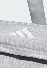 Γκρι ύφασ�μα τσάντα με υφή στην επιφάνεια, με λευκό λογότυπο τριών ρίγων και αντιθετικές ραφές στα άκρα. Απλός σχεδιασμός, λειτουργικό σχήμα.