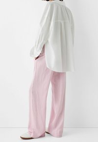White button-up shirt with long sleeves and a relaxed fit, paired with pink striped wide-leg pants and white sneakers.