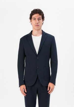 Blazer azul-marinho com dois botões e lapelas recortadas, apresentando bolsos laterais e uma textura suave. Usado sobre uma t-shirt branca de gola redonda.