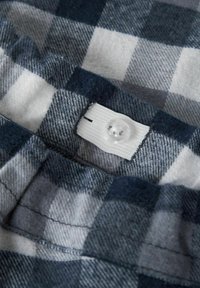 Niebiesko-szaro-szachownicza tkanina o miękkiej teksturze, z białą podszewką i przezroczystym guzikiem na górze. Widoczne detale szycia.