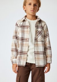 Geruite shirt in roomkleur, bruin en tan met een knoopsluiting aan de voorkant, een borstzak en een zachte, textuurstof. Draagt over een roomkleurige trui.