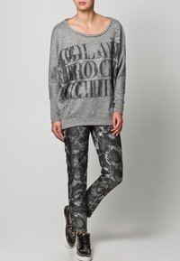 Szary, długi rękaw, bluza z czarnym tekstem i wzorami, zestawiona z czarno-białymi spodnimi z wzorami. Oba elementy mają luźny krój i miękką fakturę.