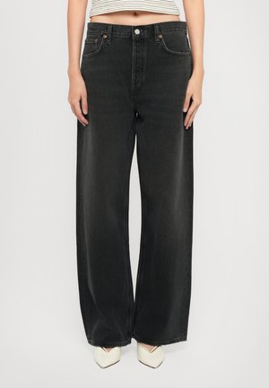 Woman wearing high-waist wide-leg black jeans with five pockets and a cropped striped top, paired with white pointed-toe shoes.