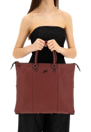 Donna in abito nero senza spalline con una grande borsa tote in pelle marrone con doppio manico e chiusura con cerniera superiore.