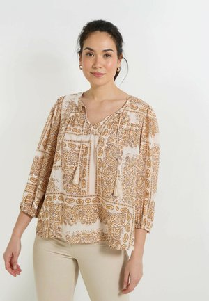 Chemisier léger à manches longues en crème avec un motif paisley orange et or intriqué. Présente un décolleté en V et des liens à pompons.