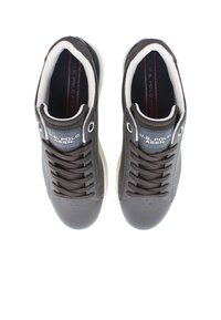 Tmavě hnědé tenisky vyrobené z kůže s hladkým povrchem. Mají bílé podrážky, kulaté tkaničky a detaily s logem na jazyku.