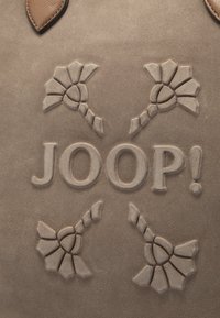 Borsa in pelle beige con motivi floreali in rilievo e la parola "JOOP!" in grande formato, con dettagli testurizzati aggiuntivi attorno al logo.