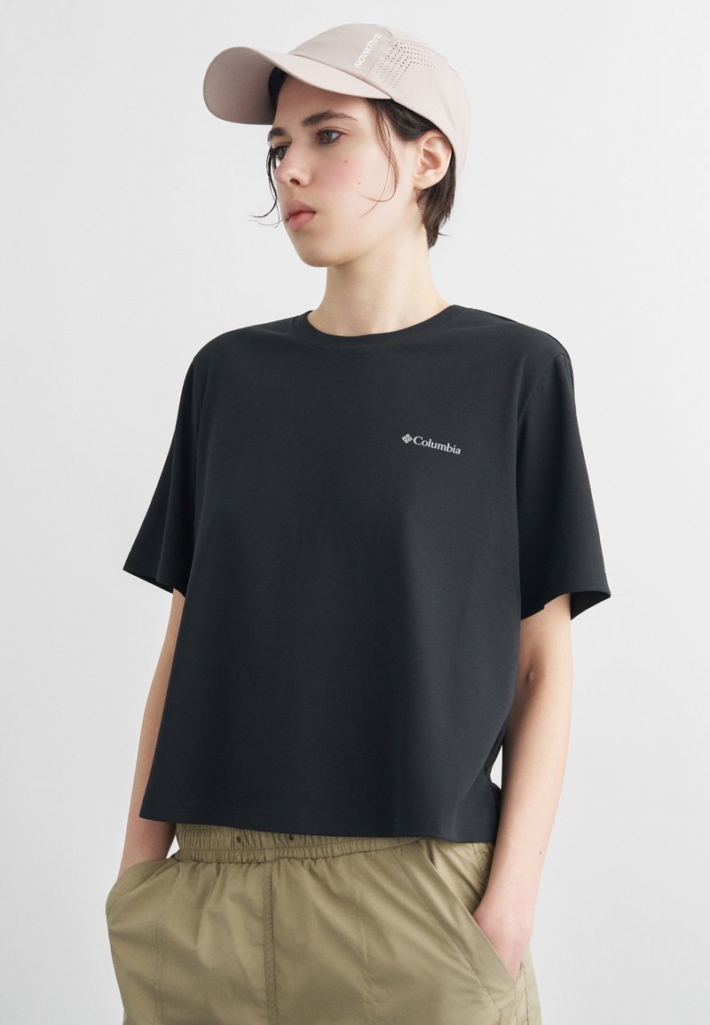 Νεαρός που φοράει μπεζ καπέλο, μαύρο t-shirt Columbia και χακί παντελόνι με τα χέρια στις τσέπες, στραμμένος ελαφρώς προς τα αριστερά σε λευκό φόντο.