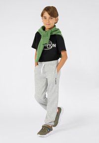 Zwarte t-shirt met "Champion" logo, lichtgrijze sweatpants, groene trui om de nek geknoopt, en olijfgroene sneakers met witte zolen.