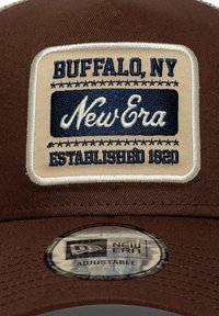 Καφέ καπελάκι με μπεζ λεπτομέρεια που φέρει μπλε κεντημένο κείμενο: «Buffalo, NY», «New Era» και «Established 1920». Ρυθμιζόμενος ιμάντας κάτω από το γείσο.