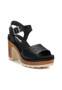 Sandalias de plataforma negras con parte superior de cuero perforado, correa ajustable en el tobillo y un tacón grueso en color beige y marrón. Plantilla texturizada.