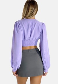 Blusa corta lilla con maniche lunghe e gonfiate, vita smock aderente, abbinata a una mini gonna grigia. Tessuto morbido, design semplice.