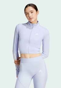 Gaiši purpura saīsināts zipa žakets ar ribotām plecu detaļām un baltām trīs svītru akcentiem uz piedurknēm, apvienots ar atbilstošām augsto jostasvietu legingām.