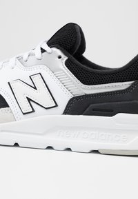 Czarno-biały but sportowy wykonany z siateczki i zamszu, z wyraźnym logo "N", teksturowanymi akcentami oraz białą podeszwą środkową.