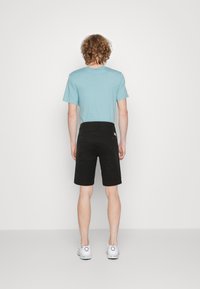 Světle modré tričko s krátkým rukávem a černé šortky, které nosí osoba zezadu. Outfitu vévodí bílé tenisky. Jednoduchý, ležérní design.