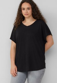 Zwarte V-hals t-shirt met korte mouwen, gemaakt van zachte stof. Ontspannen pasvorm, minimaal ontwerp en rechte zoom. Draag het met lichtgrijze spijkerbroek.