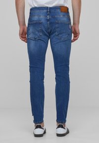 Kék farmer skinny farmernadrág közepes derékkal, öt zsebbel, bőrhiba a hátsó részén és finom halványodással az anyagon.