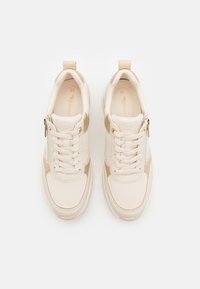 Beige sneakers med en glatt og teksturert overdel, med lisser og glidelås. Størrelsesetikett synlig, polstret krage for komfort.