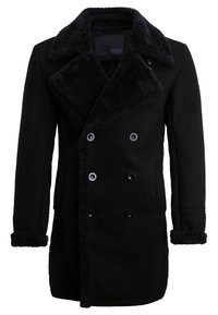 Manteau noir croisé à double boutonnage avec un col et des poignets en fourrure noire texturée, tissu lisse et boutons ronds noirs.