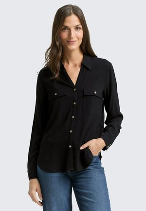 Chemise noire à manches longues avec fermeture à boutons, deux poches poitrine et accents en bouton argenté. Tissu lisse, col féminin et coupe décontractée.