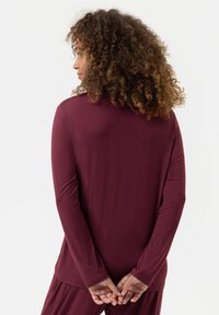 Bordeaux lange mouwen top van zachte stof. Heeft een ronde halslijn en een rechte zoom met fitted mouwen. Geen zichtbare patronen of accenten.