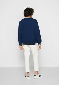 Sweatshirt bleu marine avec un col rond, des poignets et un ourlet côtelés, associé à un pantalon blanc retroussé et des baskets claires.