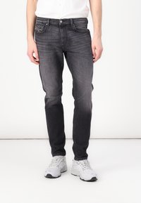 Jean en denim gris foncé à coupe slim, design à cinq poches et texture légèrement délavée. Assorti avec des baskets gris clair.
