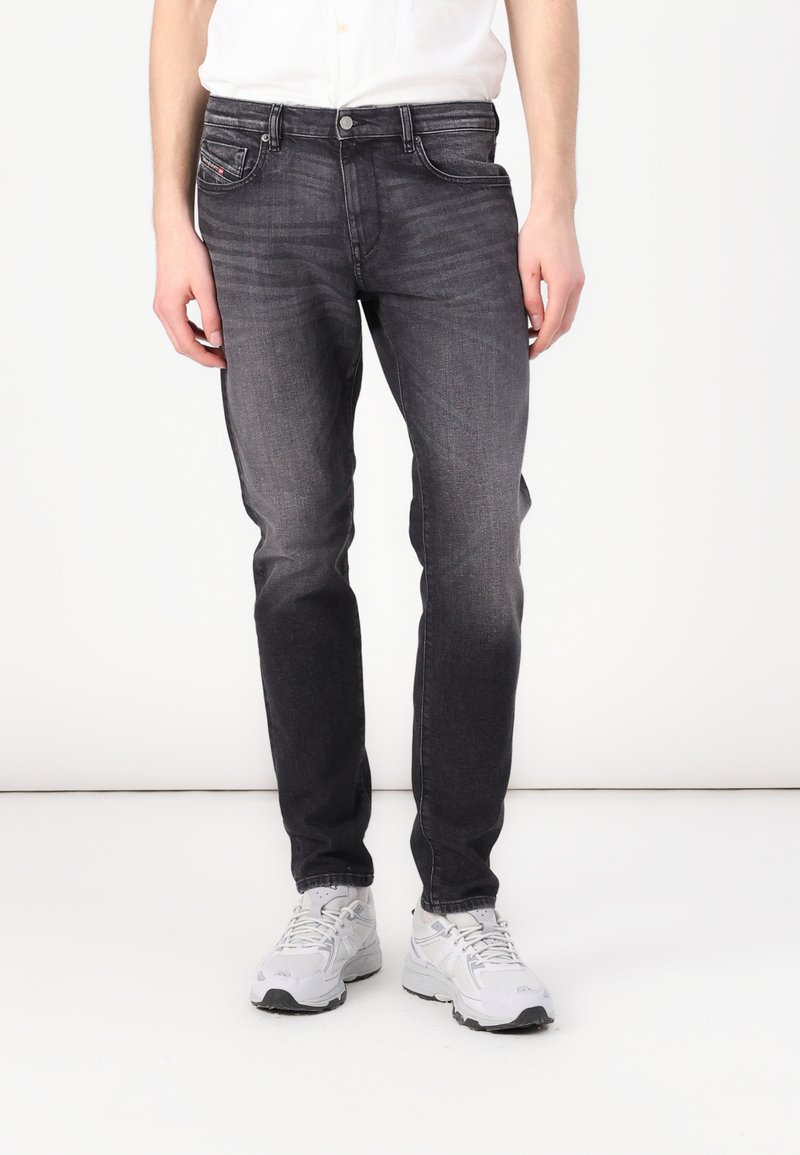 Jean en denim gris foncé à coupe slim, design à cinq poches et texture légèrement délavée. Assorti avec des baskets gris clair.