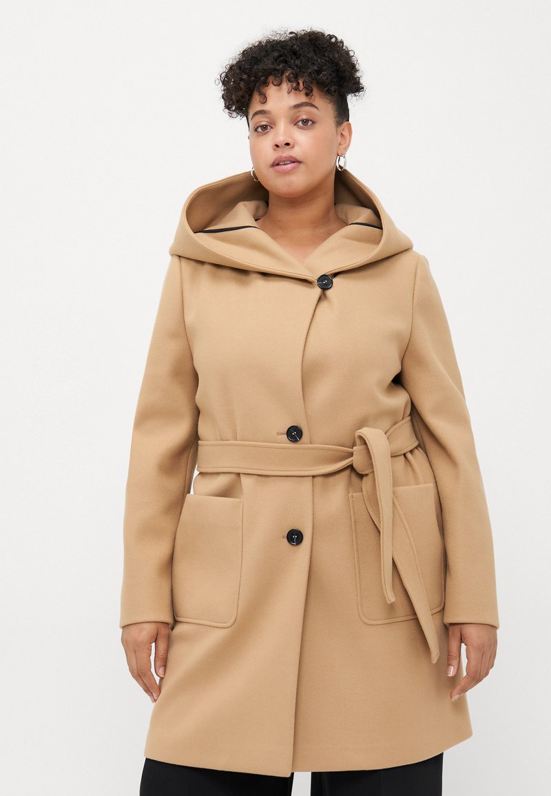 Beige ullblandingsfrakk med stor hette, to frontlommer, svarte knapper og belte med egen knyting. Glatt tekstur og skreddersydd design.