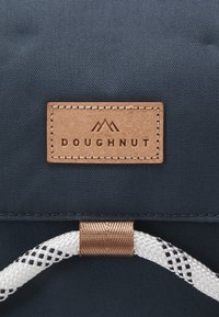 Ruskea nahkalaatta, jossa on ommeltu reuna ja "DOUGHNUT"-teksti tummansinisen kankaan päällä, valkoisen ja mustan köysilenkin päässä.