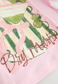 Tissu rose avec une illustration d’un verre à martini rayé vert et blanc, deux olives vertes, un nœud rose et le texte « Dry Martini » en cursive marron.