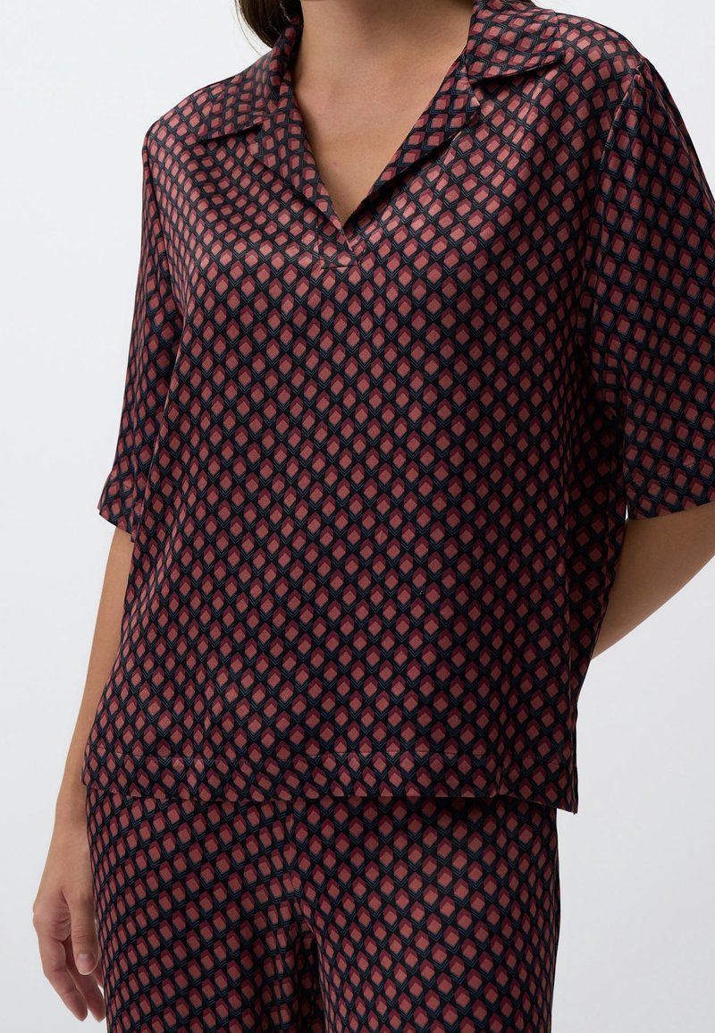 Femme portant un haut à manches courtes et un pantalon assortis avec un motif géométrique en losange rouge foncé et bleu marine.