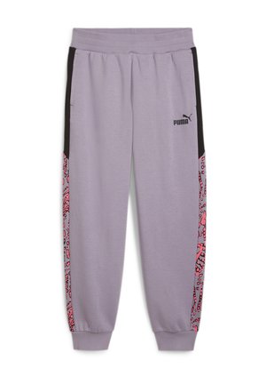 Person iført en lilla Puma træningsdragt med pink og sort abstrakt mønster på toppen og side striber, hvide sneakers, stående mod en grå baggrund.