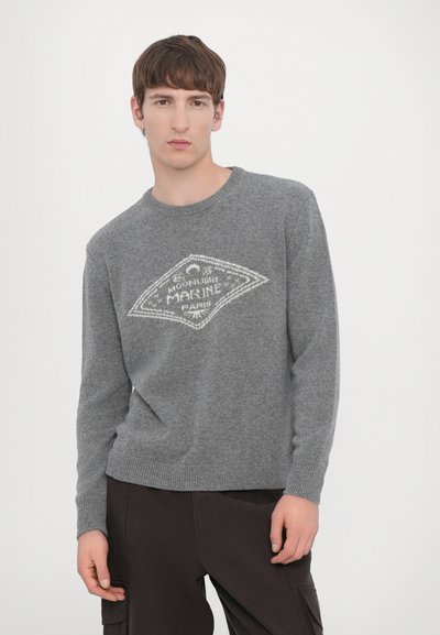 Pull en maille grise avec un col rond et des poignets côtelés. Présente un motif de losanges blancs et un design textuel sur le devant.