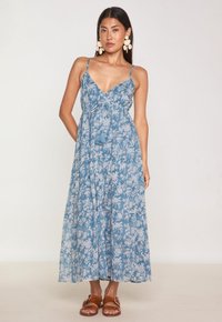 Robe maxi florale bleue avec des bretelles spaghetti, taille à nouer et jupe à volants. Fabriquée en tissu léger avec une texture douce et un accent en pampille.