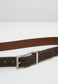 Brauner Leder Gürtel mit glatter Textur, ausgestattet mit einer silbernen Metall Schnalle, weißen Nähten und mehreren Einstelllöchern.