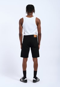 Shorts de mezclilla negra de corte recto, combinados con una camiseta sin mangas blanca. Los shorts presentan un parche de cuero marrón en la cinturilla trasera.