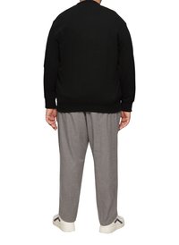 Czarny sweatshirt z okrągłym dekoltem, w zestawieniu z jasnoszarymi spodniami w kant i białymi sneakersami z granatowymi akcentami. Gładkie tło.