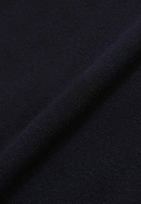 Gros plan d'un tissu tricoté bleu marine foncé avec une texture visible et un pli diagonal sur la surface.