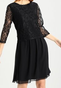 Svart knälång klänning med blommig spetsliv och trekvartsärmar i spets, kombinerad med en svängd chiffongkjol.