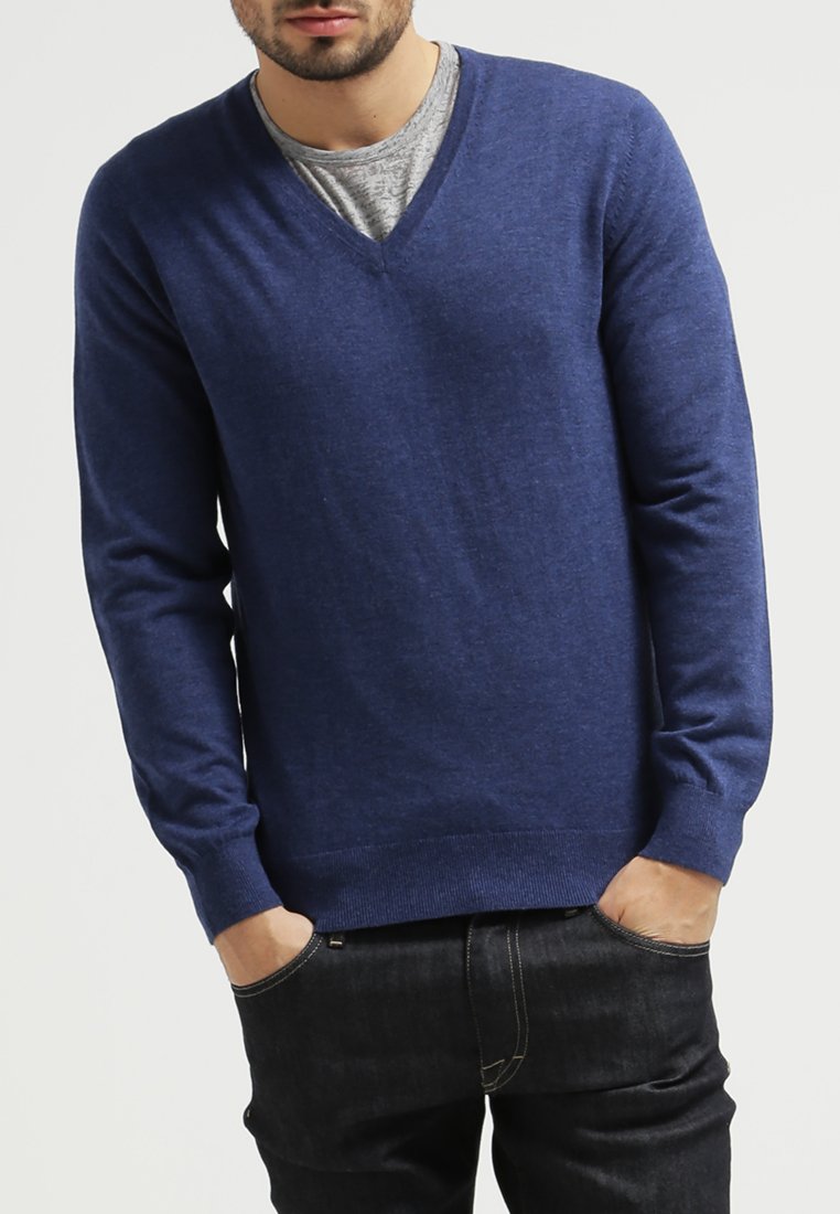 Dunkelblaues V-Ausschnitt-Pullover aus weichem Material mit langen Ärmeln, gerippten Bündchen und Saum, über einem grauen T-Shirt getragen, kombiniert mit dunklen Jeans.